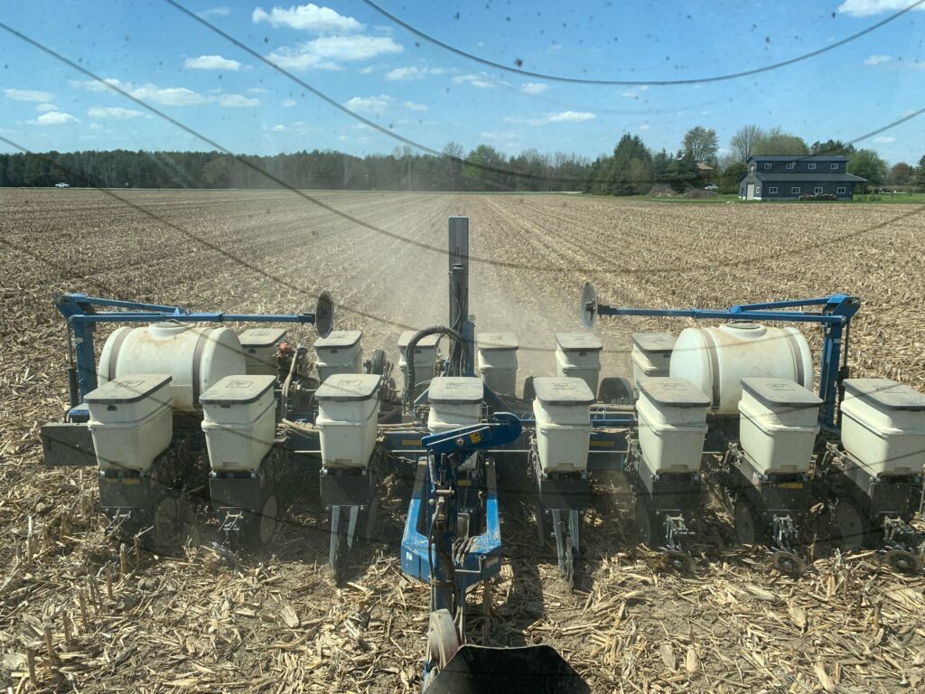 A planter operating in a field of corn residue, with trees in the background.