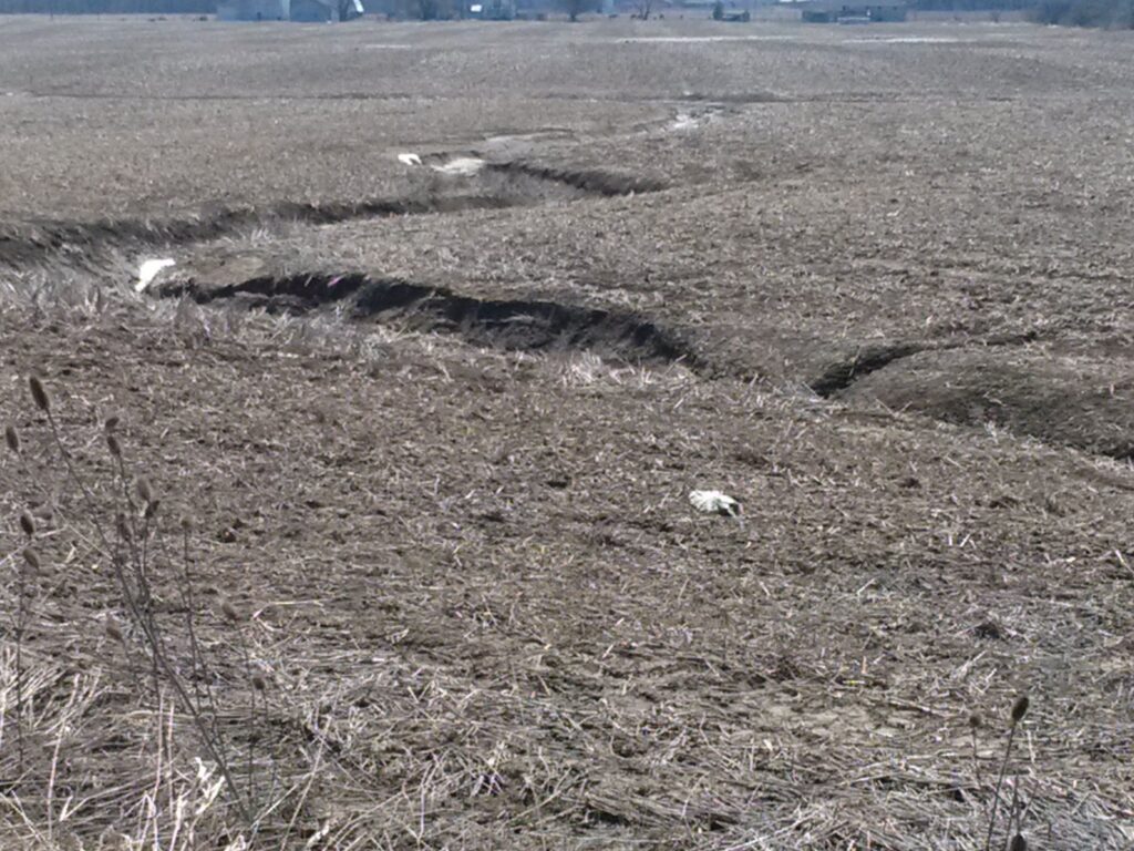 field with a deep cut in it that has some plastic wrap bales inside.